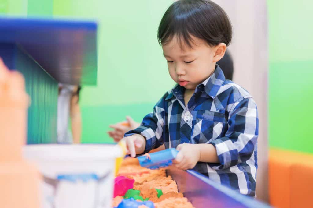 A small toddler playing with in a sand sensory bin
