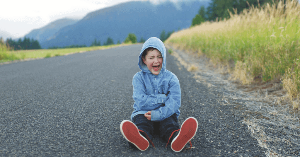Child is sitting in the middle of a road experiencing a tantrum.