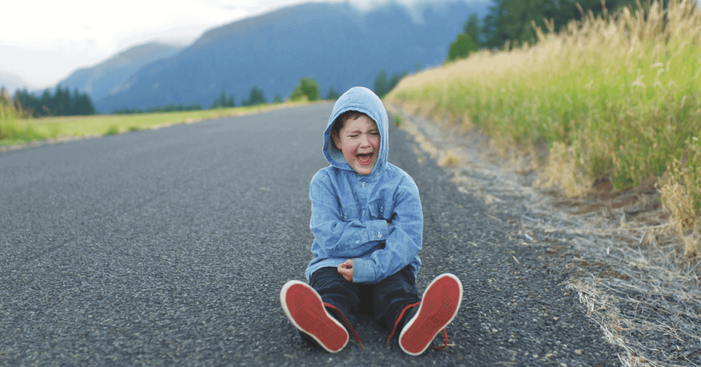 Child is sitting in the middle of a road experiencing a tantrum. 