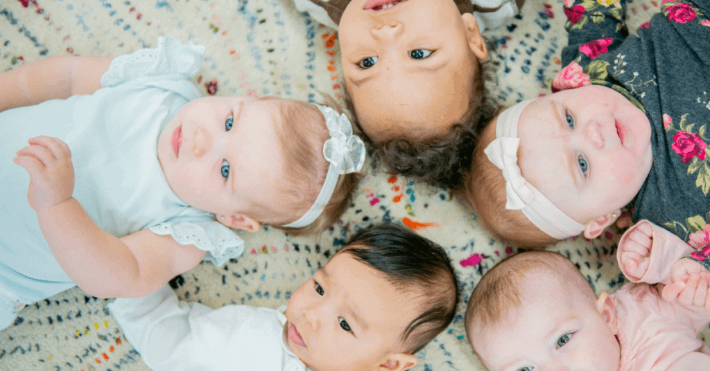 5 babies laying on Matt in a circle after the pandemic, during a baby and/or toddler group