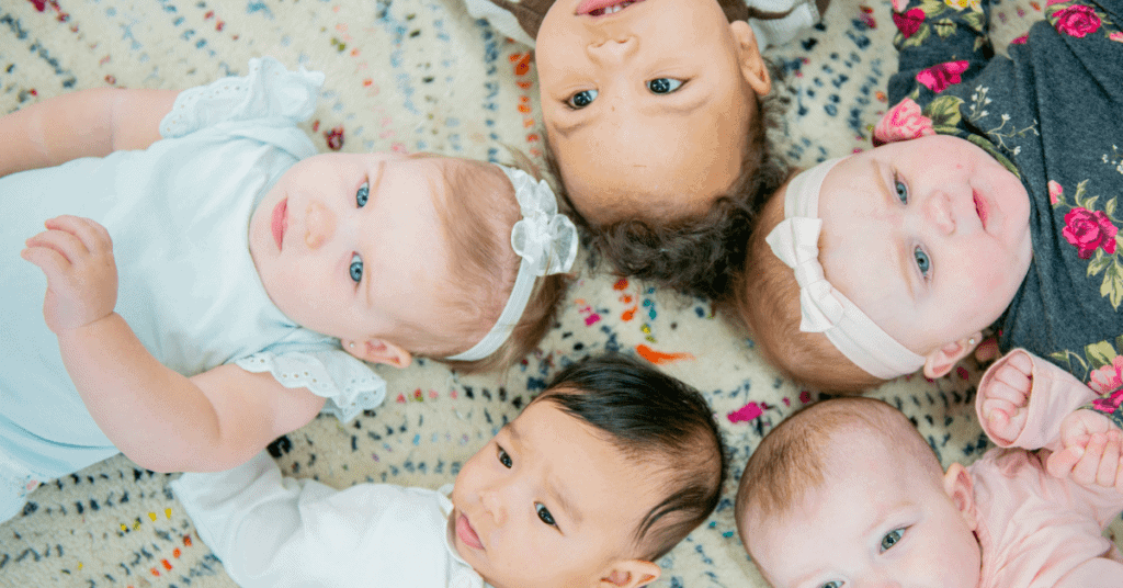 5 babies laying on  Matt in a circle after the pandemic, during a baby and/or toddler group