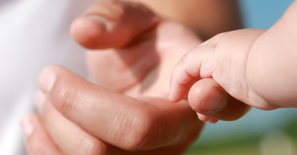 A baby's hand is gripping hold of a new dad's forefinger.