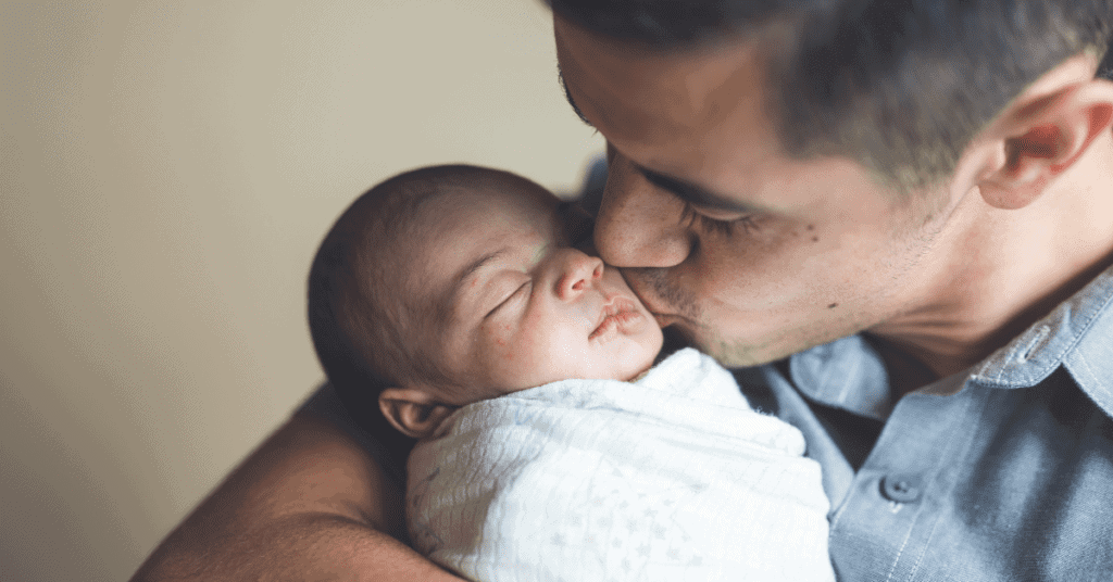 A new dad kissing their newborn baby