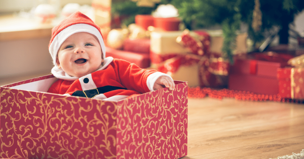 Corresponding with the baby facts, baby sits in an open gift box dressed in a Father Christmas outfit