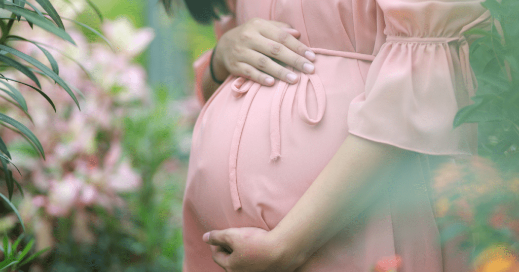 A pregnant woman stands amongst nature wearing pink.  A good environment for easing a rough day for mental health.