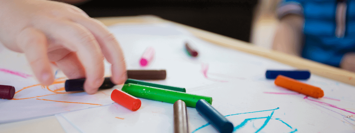 toddler making marks with crayons on a sheet of paper