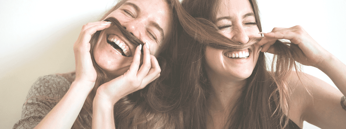 two women being silly - making moustaches from their hair and laughing together