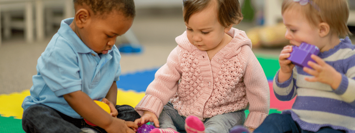 three toddler playing together and sharing toys at a baby group