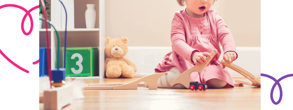 leaving a child at nursery for first time - little girl playing with a train set at nursery