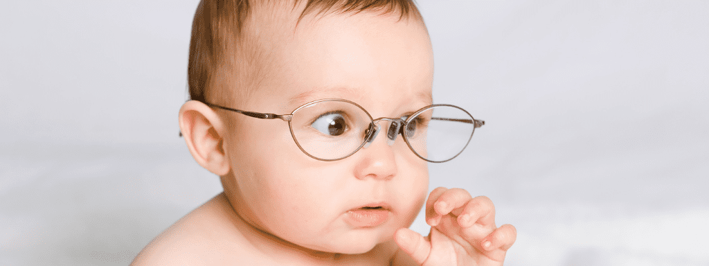 The 5 senses for a baby: to demonstrate Sight, this image shows a baby looking humorously startled while wearing a pair of glasses.