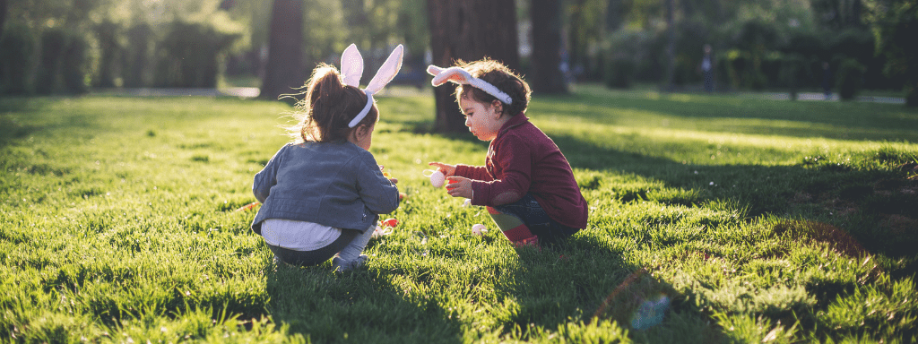 Easter Activities Toddlers: Two toddlers stand in a field holding Easter eggs and wearing bunny ears