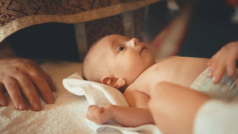 Image is of a young baby with two caregivers