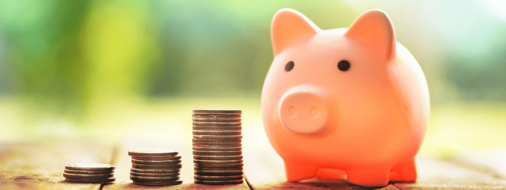 Doing school holidays on a budget: image shows a pink piggy bank next to three stacks of coins. 