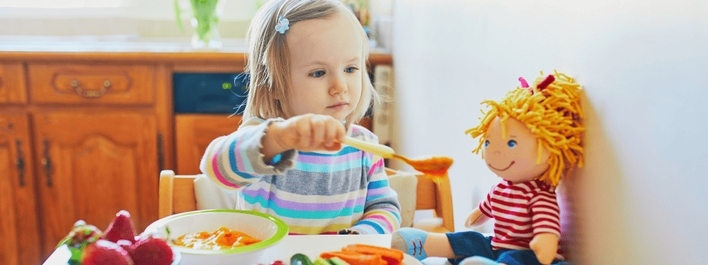 Girl playing imagination games by feeding her food to a doll