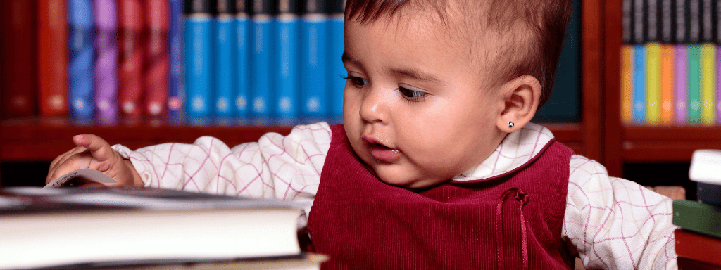 School holidays on a budget: image shows a baby in a library looking down at a stack of books and turning a page.