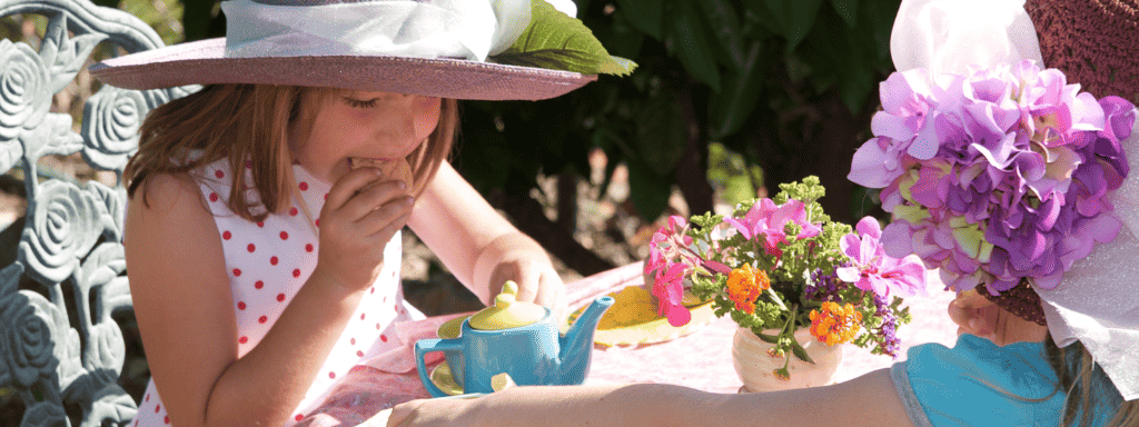 Father's day activities: have an afternoon tea! Two girls sit together eating biscuits while playing with a toy teapot.