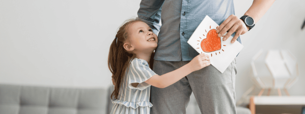 father's day activities: creating a handmade card -a little girl hugs her dads leg while giving him a handmade card