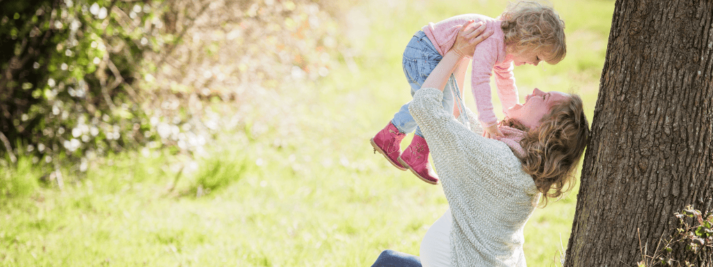 Things to do in Cardiff for families: image shows a pregnant mother holding a baby in the air while sitting in the park. 