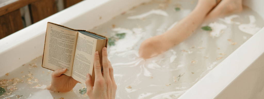 leg cramps during pregnancy - image shows a woman laid in a bath, her feet peeking out of the water, while she reads a book.