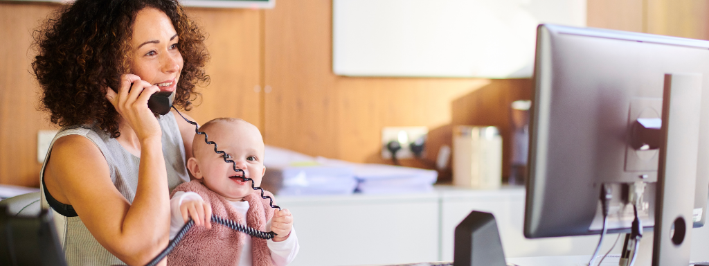 Going back to work -image shows a woman holding a baby while talking on the phone and looking at a computer