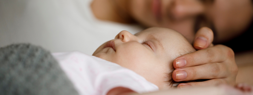 baby sleep - image shows a sleeping baby, with a parents hand gently resting on their head