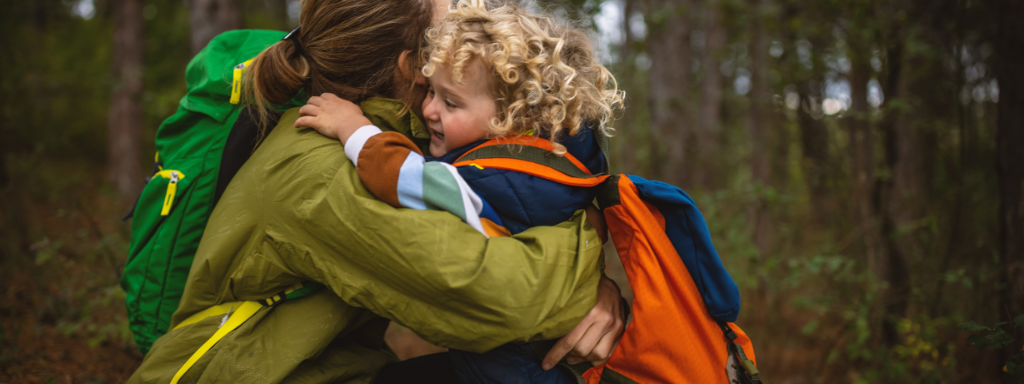 Outdoor clothing for babies - image shows a toddler and a mother both wearing backpacks, hugging.