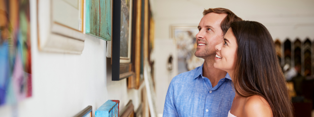 Image shows a couple in an art gallery looking at the pieces on the wall.