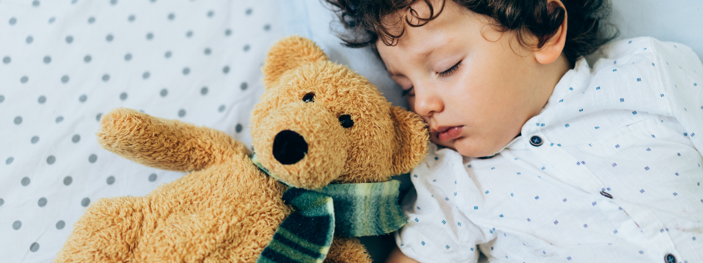 child sleep tips -image shows a child sleeping next to a brown teddy bear.
