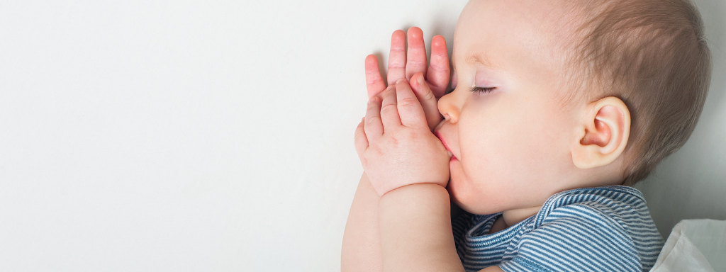 image shows a baby sleeping while sucking their thumb