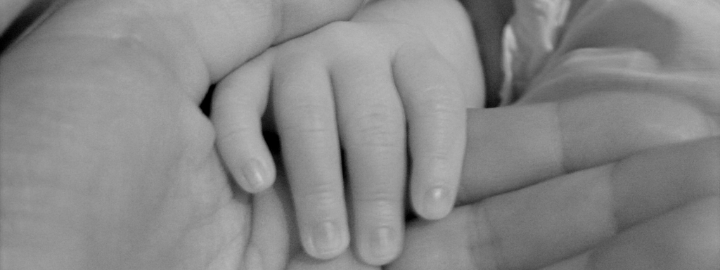 Black and white image of a baby hand being held by an adult