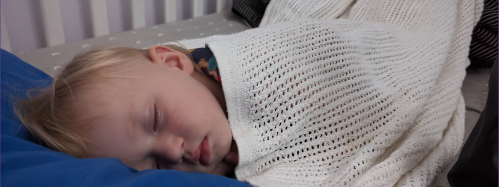 Toddler sleeps in a toddler bed with a white blanket over her