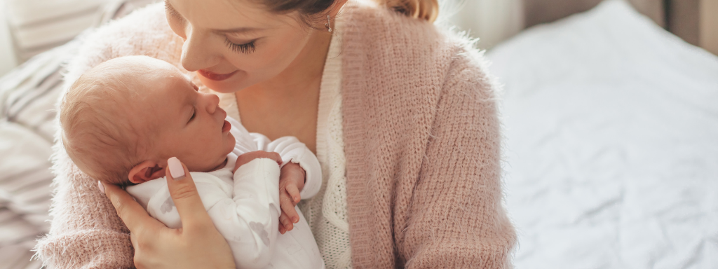 A mum cuddles a young baby as they sit on a bed