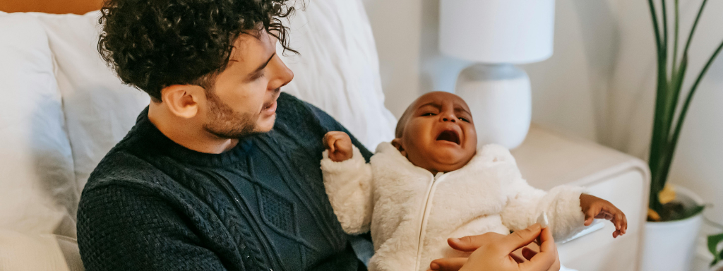 A baby cries as they are cuddled on a bed