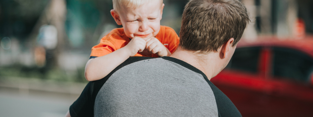 An anxious toddler holds onto his dad's shoulder