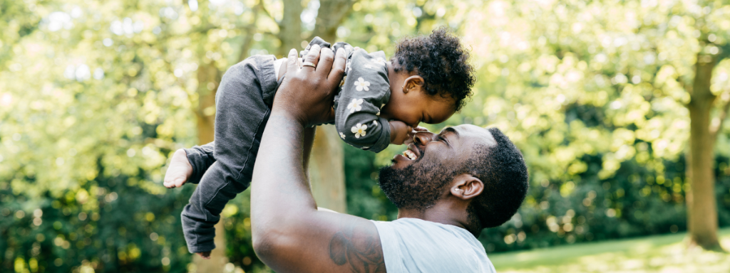 A dad holds up a toddler and they touch noses happily