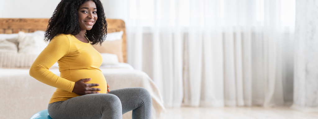 A pregnant lady smiles as she sits on an exercise ball