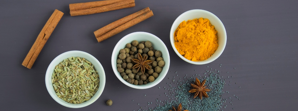 Herbs and spices are in bowls on a table, with some cinnamon sticks and star anise on the side. 