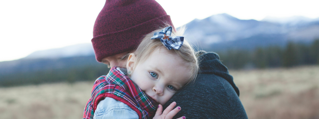 A toddler looks thoughtfully at the camera as she is cuddled