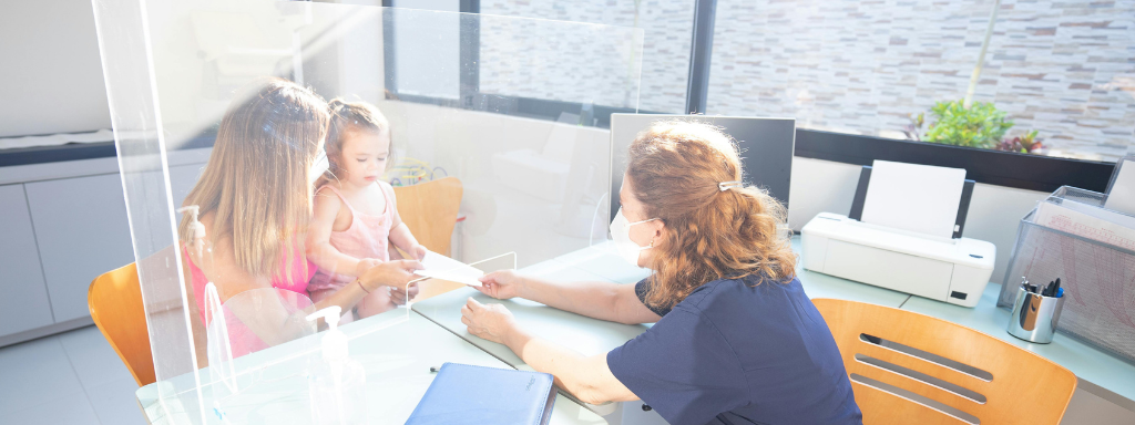 A mum and toddler sit behind a Perspex screen to talk to a health visitor 
