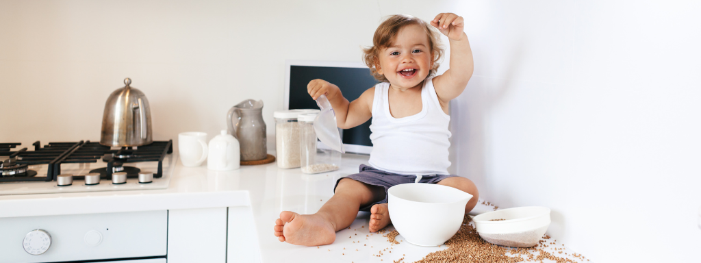 getting children involved in the ktichen - image shows a toddler sitting on a counter putting grains into a bowl