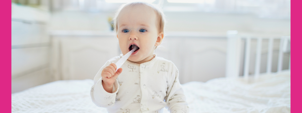 A baby dressed in white brushes its teeth