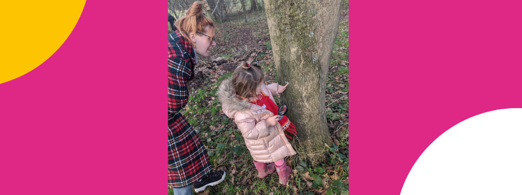 A toddler looks at a tree, magnifying glass in hand 