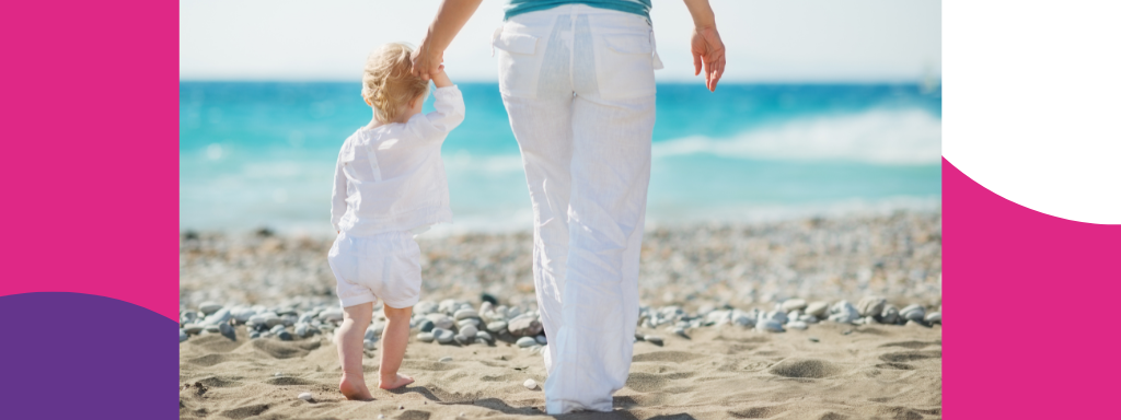 A women hold hands with a toddler as they walk on a beach