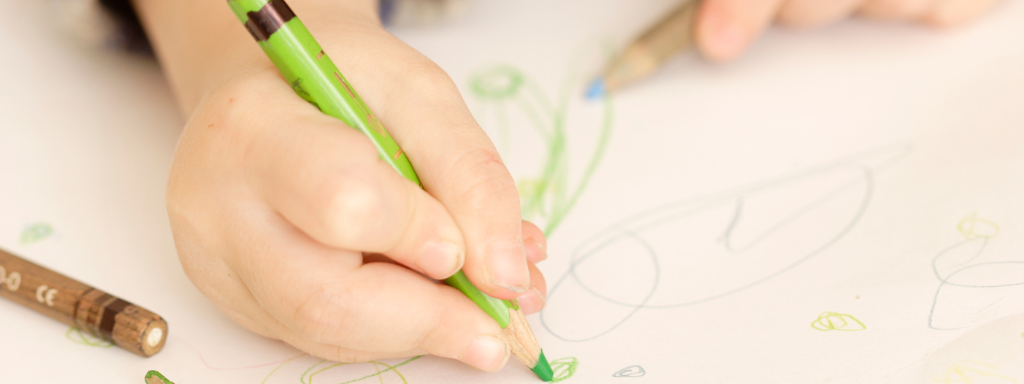 A child writes with a green crayon