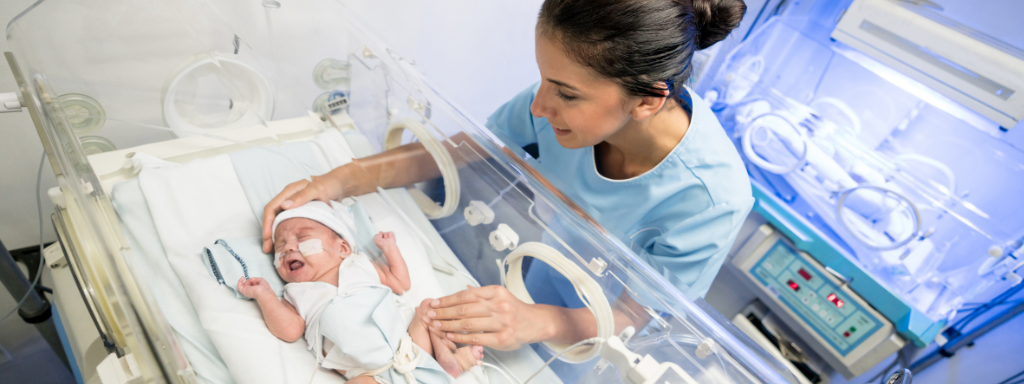 A lady smiles as she looks at and strokes a baby in an incubator