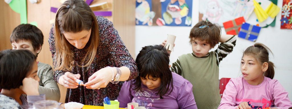 Children are doing some crafts, with a teacher helping them