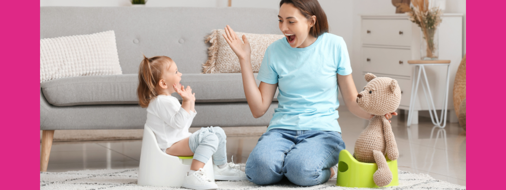 A mum and toddler smile as the toddler sits on a potty, a teddy also sits on a potty nearby