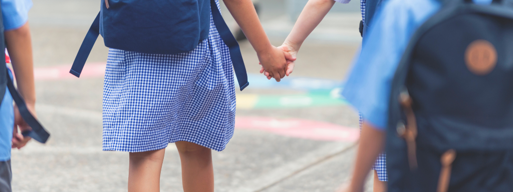Children in school uniform hold hands, seen from behind