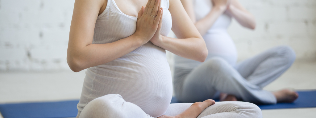 pregnancy classes - the image shows two pregnant women sitting cross-legged on the floor with their hands in a yoga pose