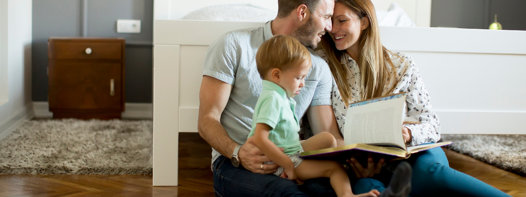 parenting books - the photograph shows a man, woman and child sitting together reading a book.